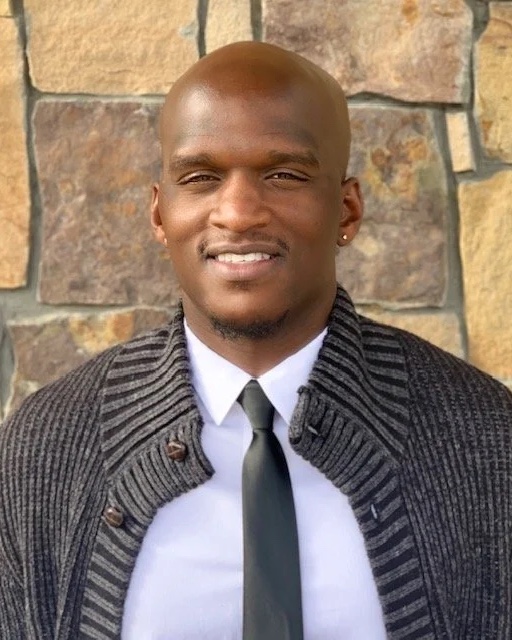 Demetrius Biggs, LPC, in a grey cardigan and tie, photographed outdoors